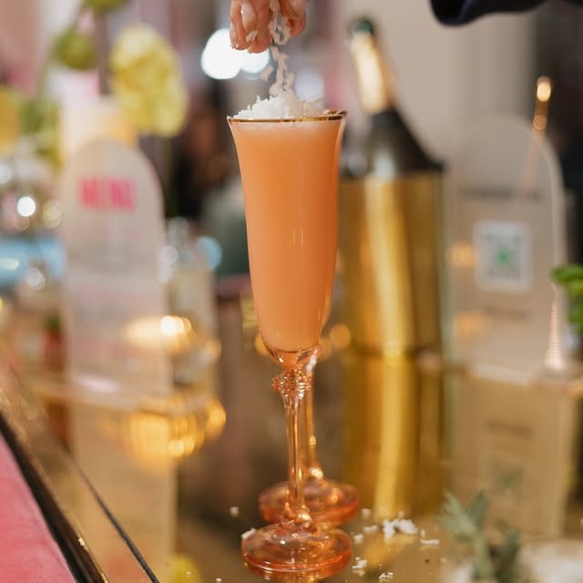 A peach cocktail in a tall flute on a mirrored bar