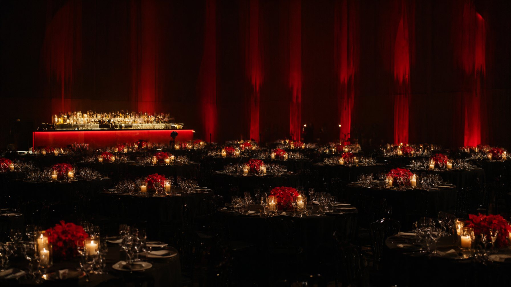 A grand ballroom dressed in black linen, red florals and candlelight before guests arrive